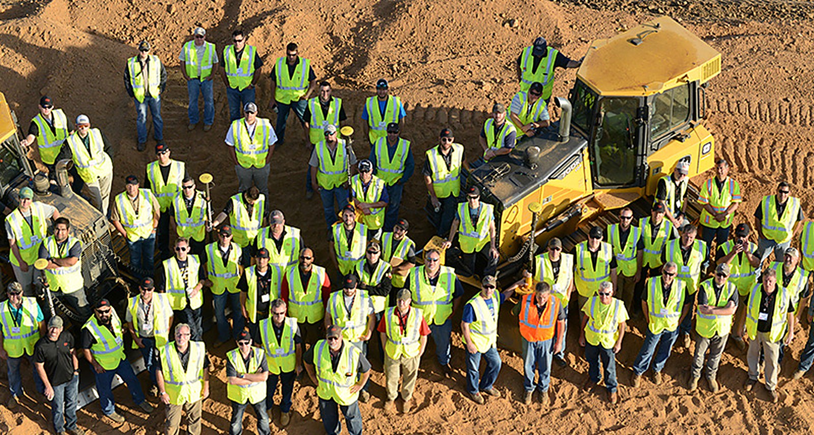 Large team in high-visibility vests gathered around a dozer on a construction site